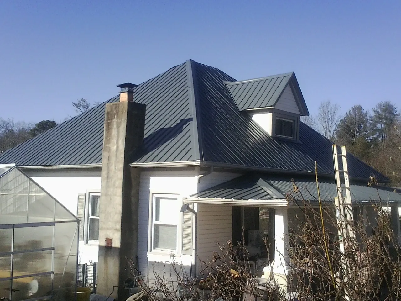 Dark blue standing seam metal roof on a white farmhouse with dormer — Slate & Tile Roof Repair by Roofing Brothers in Tenafly