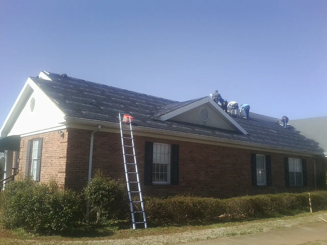 Crew tearing shingles off a brick ranch roof with a ladder set — Metal Roof Repair work by our crew in Tenafly