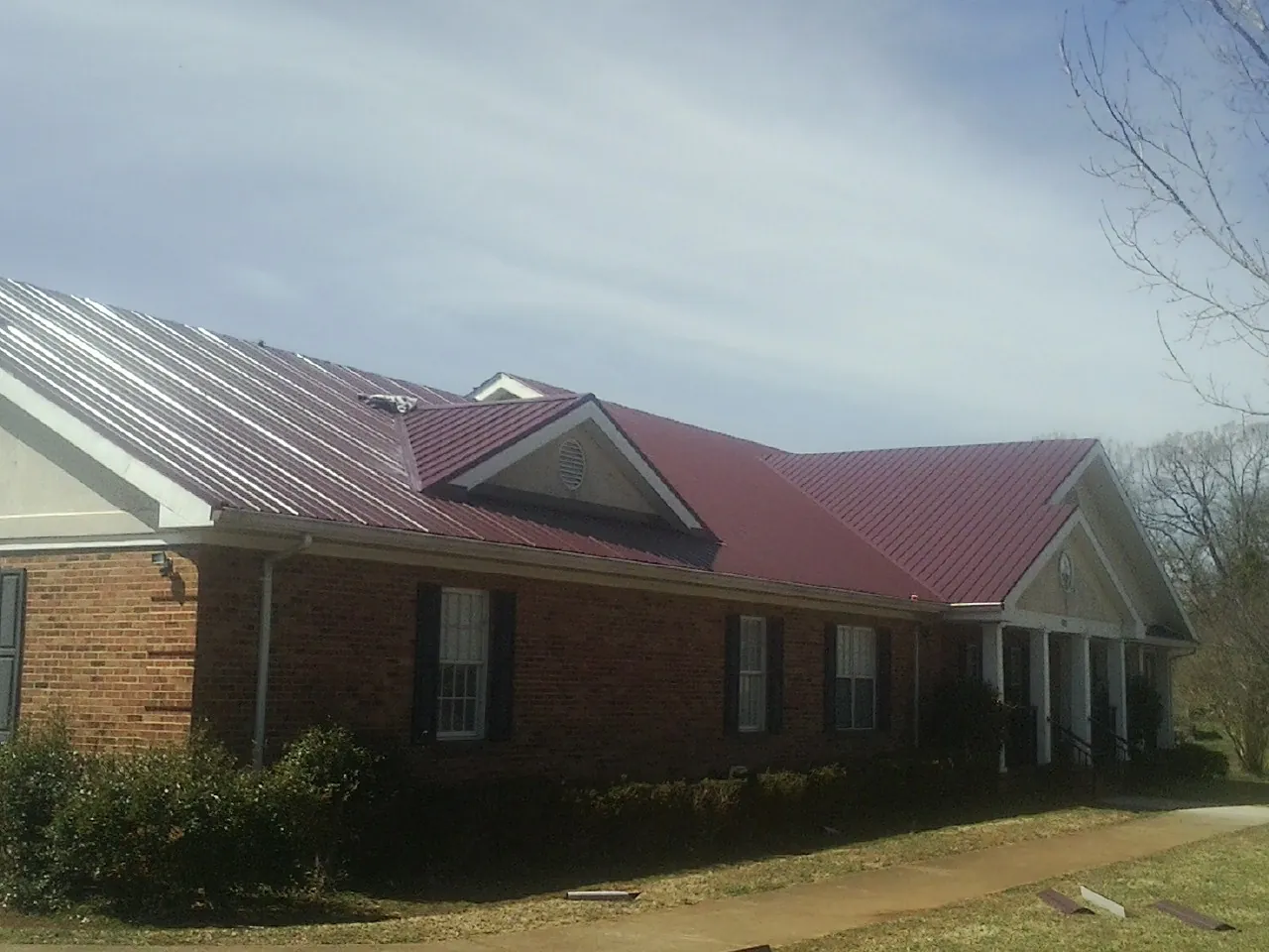 Red metal roof with gabled entries on a long brick building, from a Hail Damage Roof Repair job in Tenafly