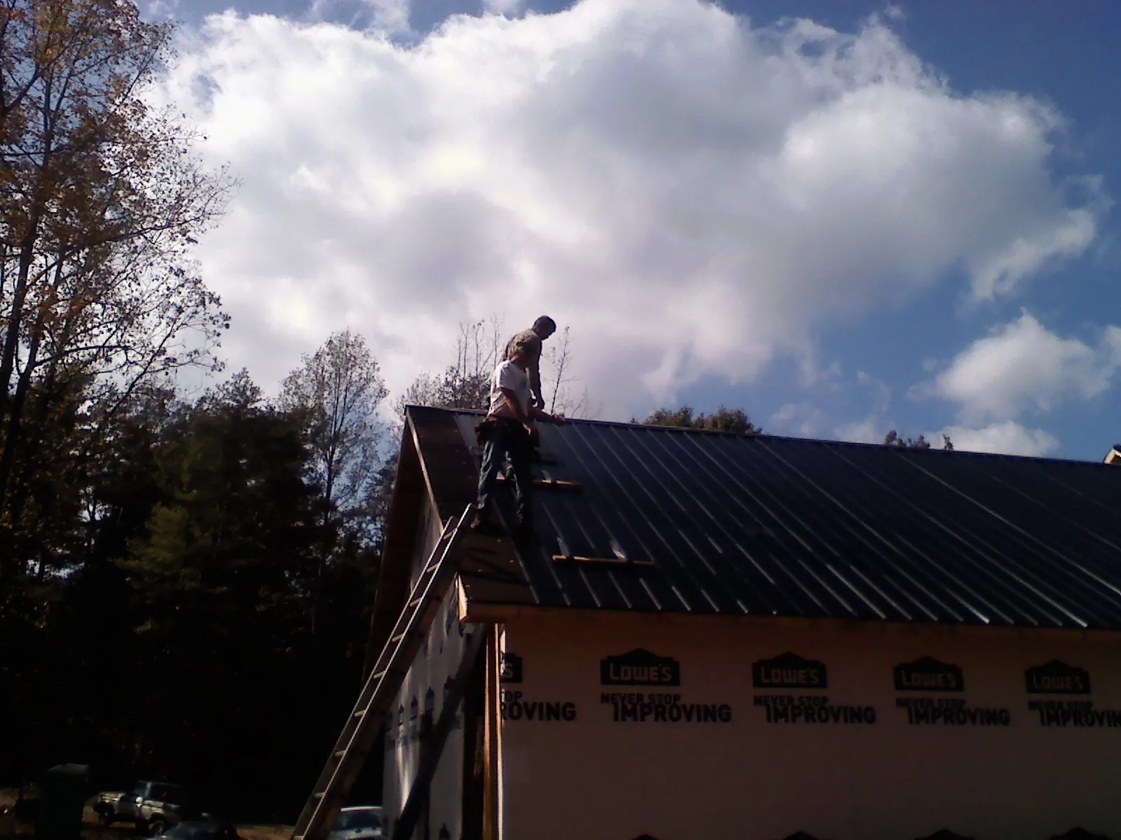 Roofer fastening dark metal panels high against a cloudy sky, from a Roof Inspection job in Tenafly